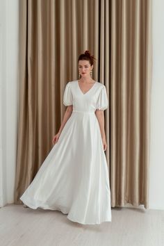 a woman standing in front of a curtain wearing a white dress with ruffle sleeves