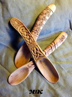 three wooden spoons with designs on them laying on a bed sheet, one is made out of wood and the other has carved handles