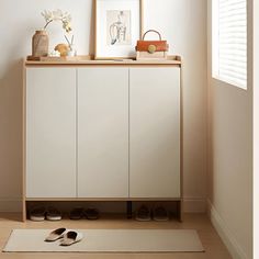 a white cabinet with shoes on the floor in front of it and an art piece