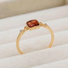 a yellow gold ring with an orange stone and diamonds on it's sides, sitting on a white surface