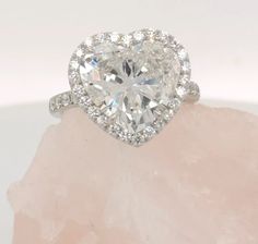 a heart shaped diamond ring on top of a pink rock with diamonds around the band