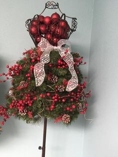 a christmas tree decorated with red ornaments and bows on top of a wooden stand in front of a white wall