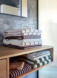 stack of folded towels sitting on top of a wooden shelf in front of a mirror