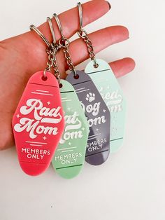 three keychains with the words real mom and member only on them are being held by a person's hand