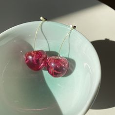 two red heart shaped glass beads sitting on top of a white bowl next to a shadow