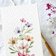 a watercolor painting of flowers on paper next to a brush