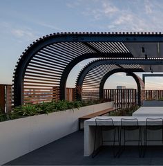 an outdoor dining area with tables and chairs under a pergolated roof at sunset