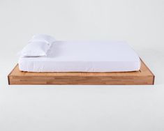 a bed with white sheets and pillows sitting on top of a wooden platform in front of a wall