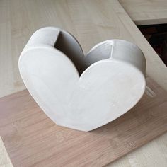 a white heart shaped vase sitting on top of a wooden table