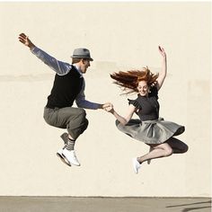 two people jumping up in the air with their arms outstretched and one person wearing a hat