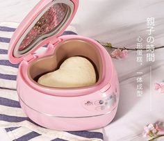 a pink heart shaped bread maker sitting on top of a table next to flowers and a towel