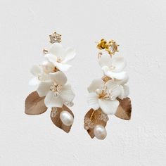 two white flowers with leaves and pearls are hanging from the side of a pair of earrings