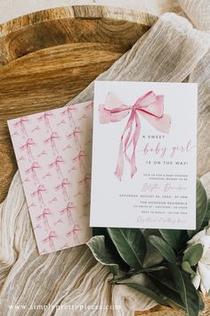 a pink and white wedding card on top of a wooden table next to some flowers