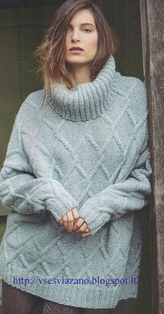 a woman wearing a gray sweater standing in front of a wooden door with her hands on her hips