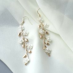 "Gold Floral Wedding earrings Gold Flower Bridal earrings Chandelier Wedding earrings Chandelier Bridal jewelry Gold Wedding jewelry These gentle bridal earrings are truly stunning and would add a romantic touch to any brides ensemble! Made from handcrafted clay flowers, 24K gold plated brass leaves they glisten and catch the light beautifully, whilst remaining classy, chic and understated. These earrings are extremely romantic! Description: - 24K Gold Plated Brass leaves - Handcrafted clay flow Floral Earrings Wedding, Flower Wedding Earrings, Bridal Gold Earrings Weddings, Gold Dangle Earrings For Wedding, Elegant Pearl Drop Danglers For Wedding, Pearl Danglers For Wedding, White Wedding Jewelry With Flower Decoration, White Flower Decoration Wedding Jewelry, Gold Danglers For Wedding