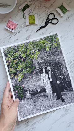 a person holding up a photo with scissors and thread on the table