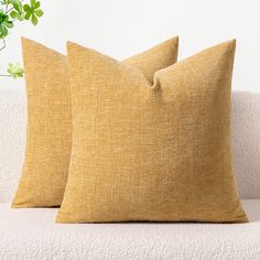 two yellow pillows sitting on top of a white couch next to a potted plant