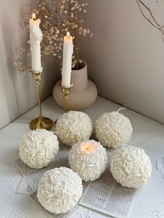 four candles are sitting next to some white flowers and small round balls with roses on them