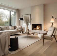 a living room filled with furniture and a fire place next to a large window on top of a hard wood floor