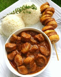 a white plate topped with meat and veggies on skewers next to rice