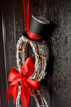 a wreath with a top hat and red bow hanging on the front door to decorate it