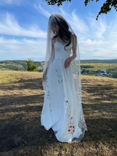 a woman in a white wedding dress is standing on the grass with her veil over her head