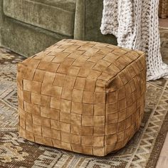 a brown square footstool sitting on top of a rug next to a green couch