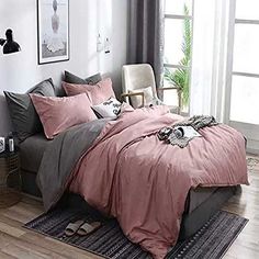 a bed with pink and grey comforters in a white room next to a window