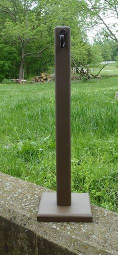 a metal object sitting on top of a cement slab in the grass next to a tree