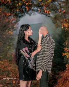 a man standing next to a woman in front of a tree with leaves on it