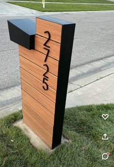 a wooden mailbox sitting on the side of a road next to a grass covered sidewalk