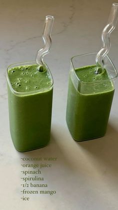 two glasses filled with green smoothie sitting on top of a white counter next to each other