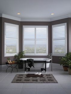 a bath tub sitting in the middle of a bathroom next to two windows with blinds on them