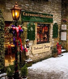 a snowy street in front of a store with christmas decorations on the windows and lights