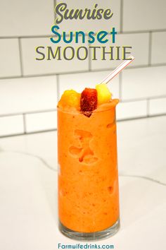 an orange smoothie in a glass with strawberries and pineapple on the rim