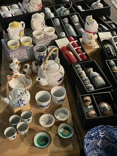 an assortment of tea cups and saucers on a table with other items in trays