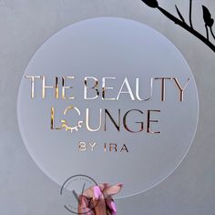 a person holding up a round sign that says the beauty lounge by ira on it