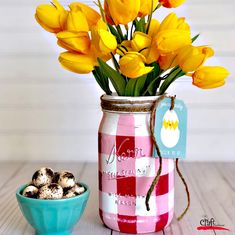 yellow tulips are in a mason jar next to a bowl of chocolate eggs