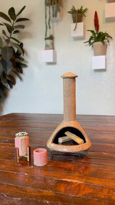 a wooden table topped with a small stove top oven next to candles and potted plants