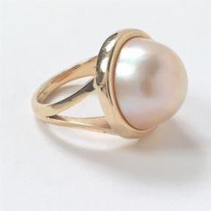 14K Yellow Gold Split Shank Mabe Pearl Ring Bezel set as the center feature is one (1) 17mm Mabe pearl with rose / cream color. Size 7.25 - 7.5 3mm 20mm x 20mm x 12mm 11.3 grams This item was appraised in March 2023 by Michael Bryant, Certified Gemologist Appraiser of Bryant and Sons, LTD. of Santa Barbara, CA.  (Picture of appraisal included in images). Please see pictures showing item details and condition. Classic Oval Ring With High Luster, Classic Oval Rings With High Luster, Oval Yellow Gold Pearl Ring With High Luster, Oval Pearl Ring In Yellow Gold With High Luster, Classic Oval High Luster Ring, Classic White Gold Cabochon Jewelry, Classic Round Pearl Ring With High Luster, 14k Stamped Fine Jewelry Pearl Ring, Oval 14k Gold Hallmarked Pearl Ring