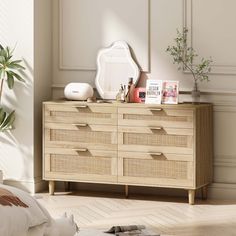 a bedroom with a dresser, mirror and plant on it's side table in front of the bed