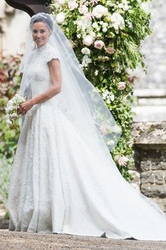 the bride is walking down the aisle in her wedding dress and veil with flowers on it