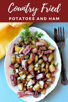 a white plate topped with potatoes and ham on top of a blue table next to a fork