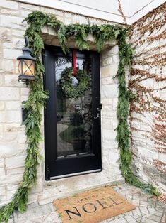 the front door is decorated for christmas with greenery on it and a welcome mat