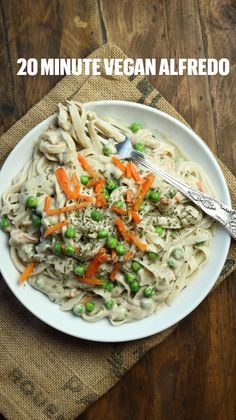 a white bowl filled with pasta and peas on top of a wooden table next to a fork