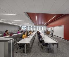 people are sitting at desks in an office with red walls and white ceilinging