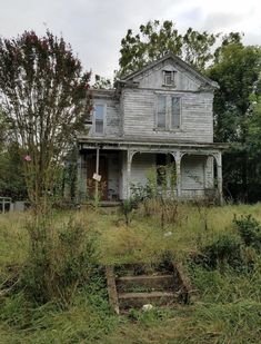 an old house sitting in the middle of a field with overgrown grass and weeds around it