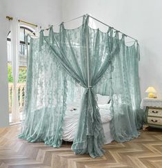 a canopy bed with sheer curtains on top of it in a room that has wooden floors and white walls