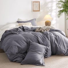 an unmade bed in a white bedroom with grey comforter and pillows on the floor