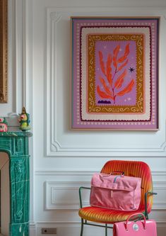 an orange chair and pink suitcase in front of a painting